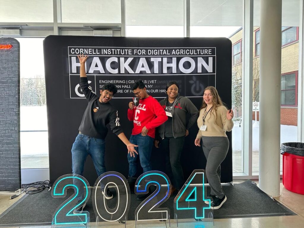 four people standing in front of large event backdrop with the numbers 2024 in the front.