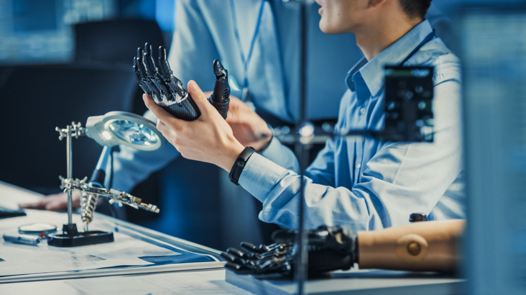 Technological Prosthetic Robot Arm is Tested by Two Professional Development Engineers in a High Tech Research Laboratory with Modern Futuristic Equipment. Man and Female Compare Data on a Personal Computer.