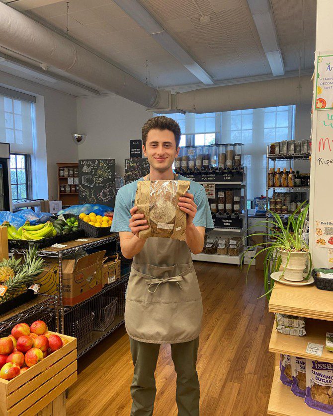 man standing in food market holding a paper bagged item