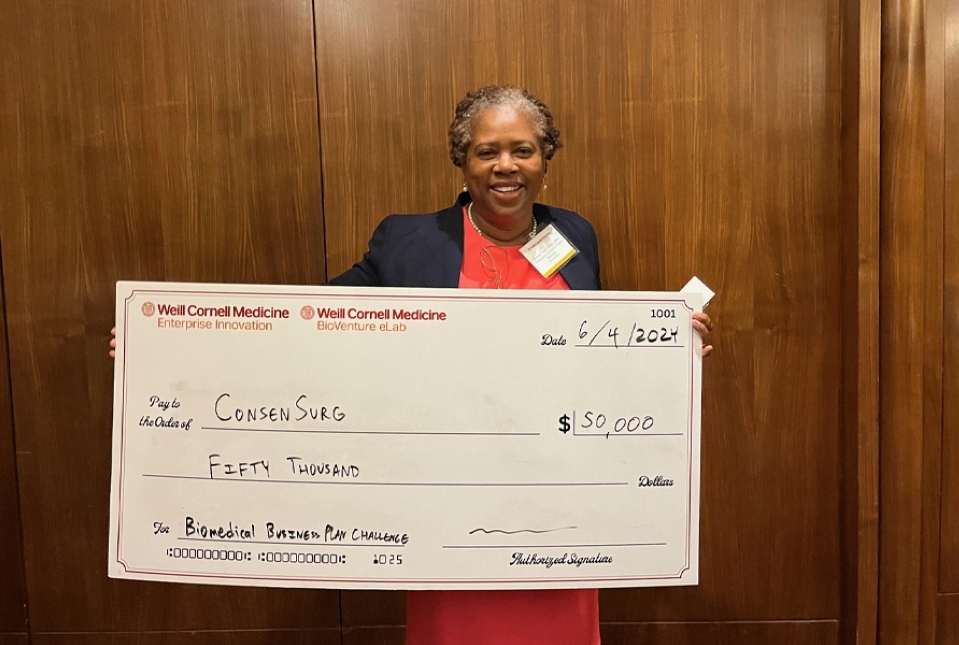 Woman wearing red dress and dark colored blazer holding $50,000 award check