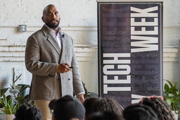 Man wearing sport coat standing next to a banner with words 