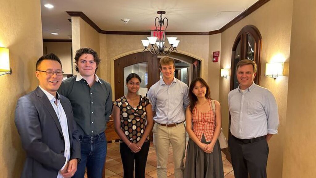 Group of people standing in a cream colored hallway looking happy.