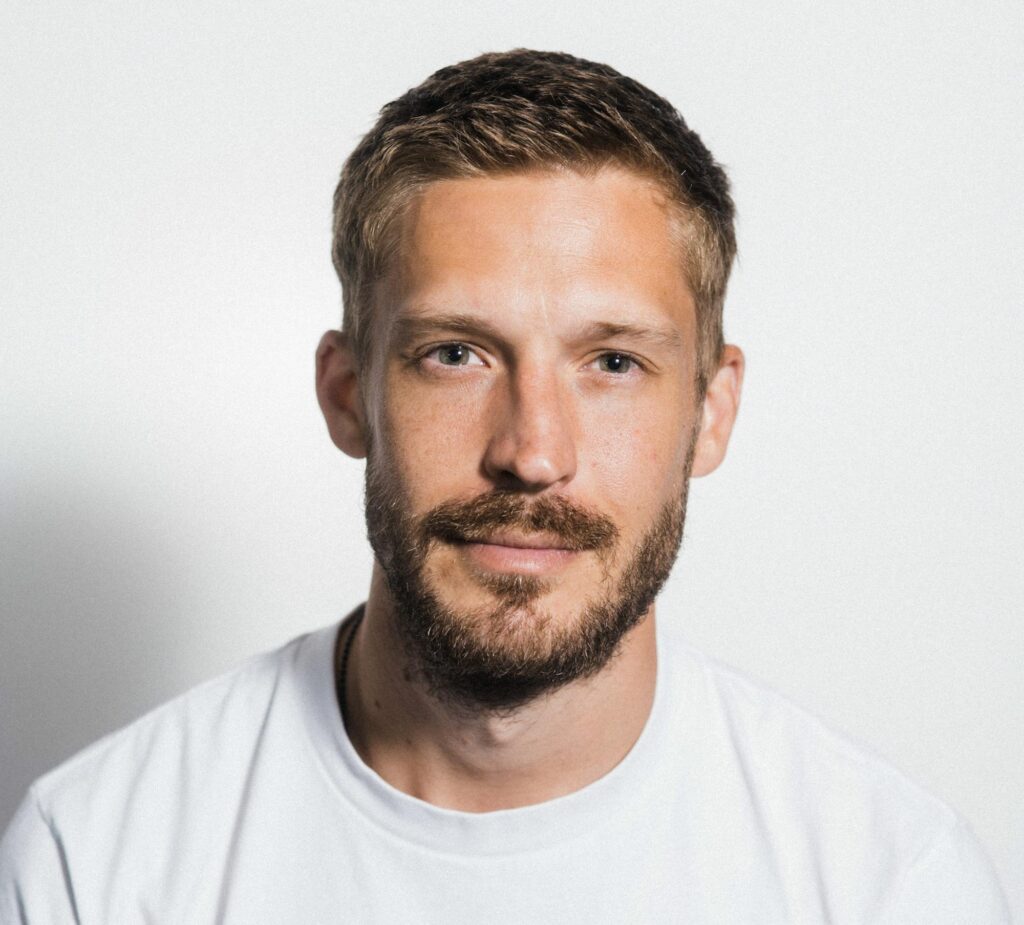 up close photo of blond haired man with facial hair wearing white shirt