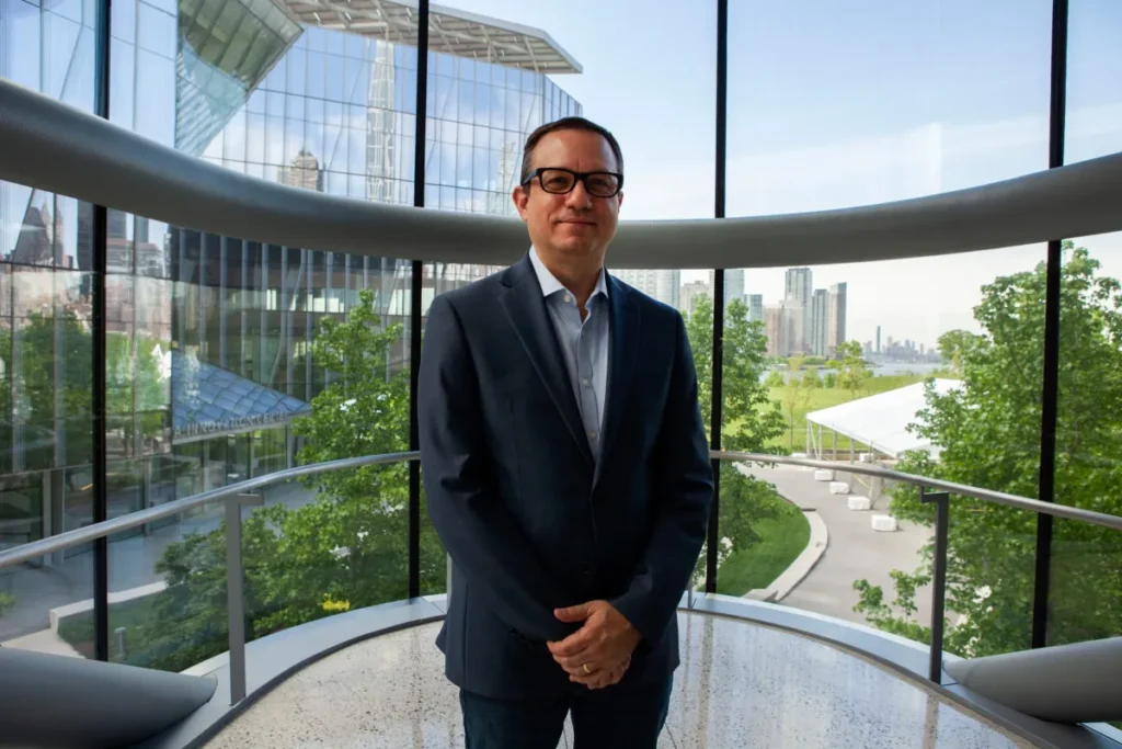 Man wearing dark suit and glasses standing in front of round glass wall skyscraper background