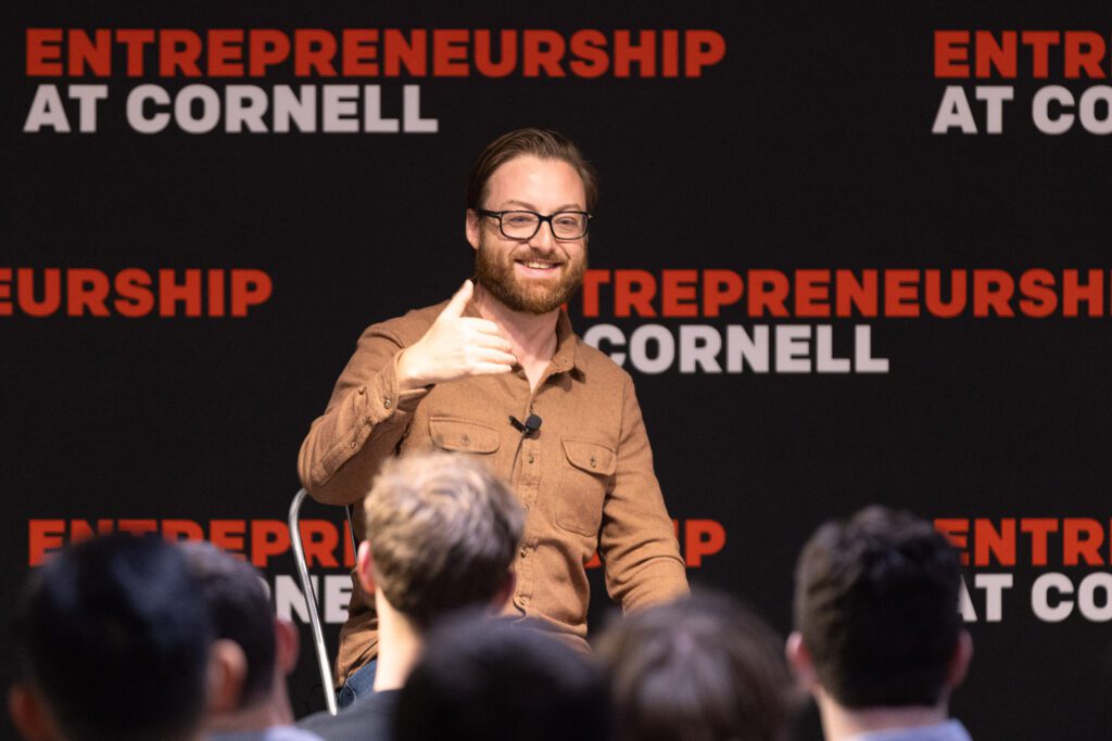 Man wearing brown shirt sitting in front of a crowd of people.
