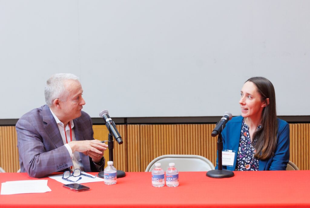man and woman sitting at a table, both speaking into a microphone