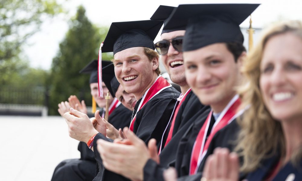 multiple people wearing black cap and gown looking to the side, smiling and clapping.