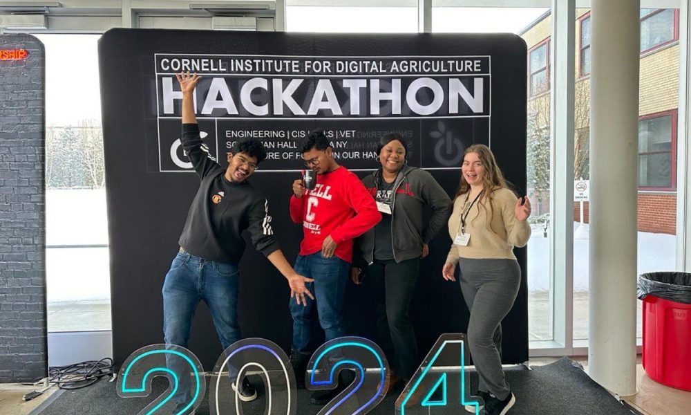 four people standing in front of large event backdrop with the numbers 2024 in the front.