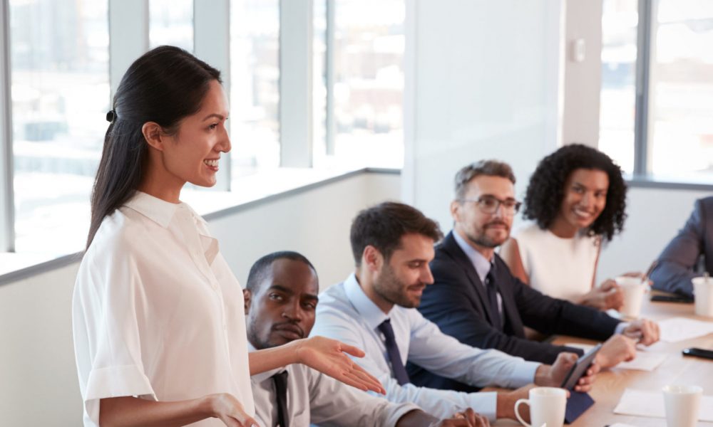 Businesswoman Stands To Address Meeting Around Board Table