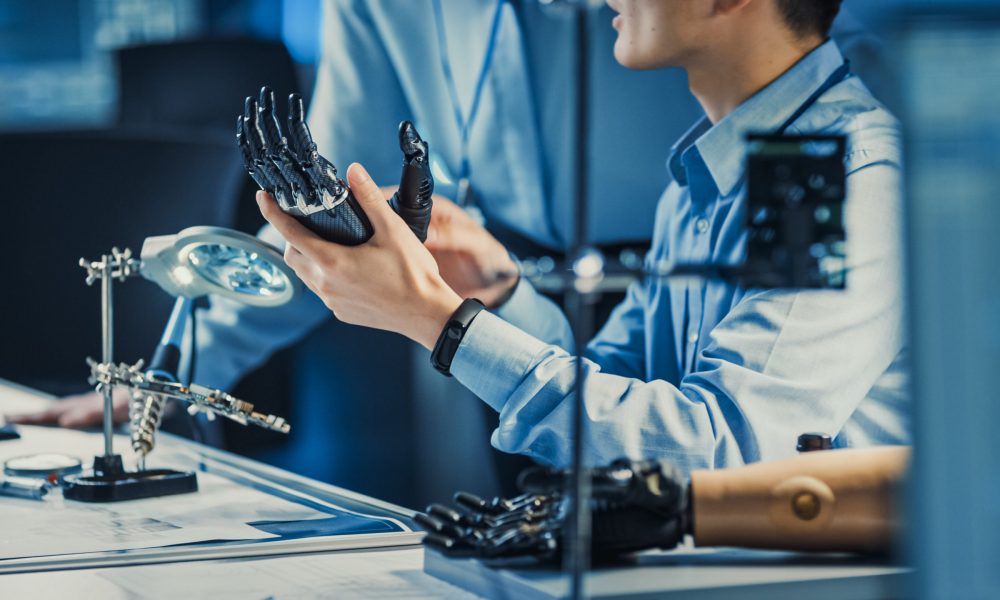 Technological Prosthetic Robot Arm is Tested by Two Professional Development Engineers in a High Tech Research Laboratory with Modern Futuristic Equipment. Man and Female Compare Data on a Personal Computer.