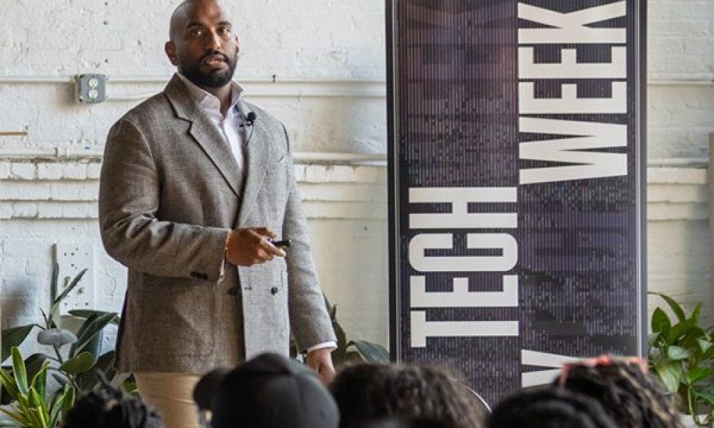 Man wearing sport coat standing next to a banner with words