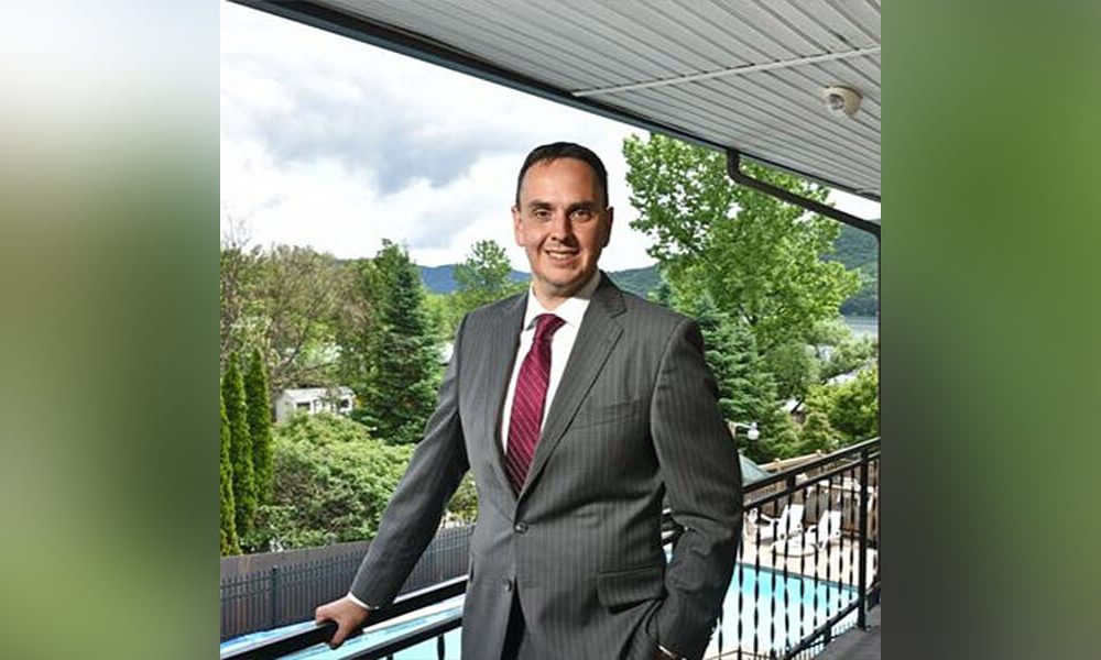Robert Gregor standing on balcony overlooking pool wearing a suit and red tie