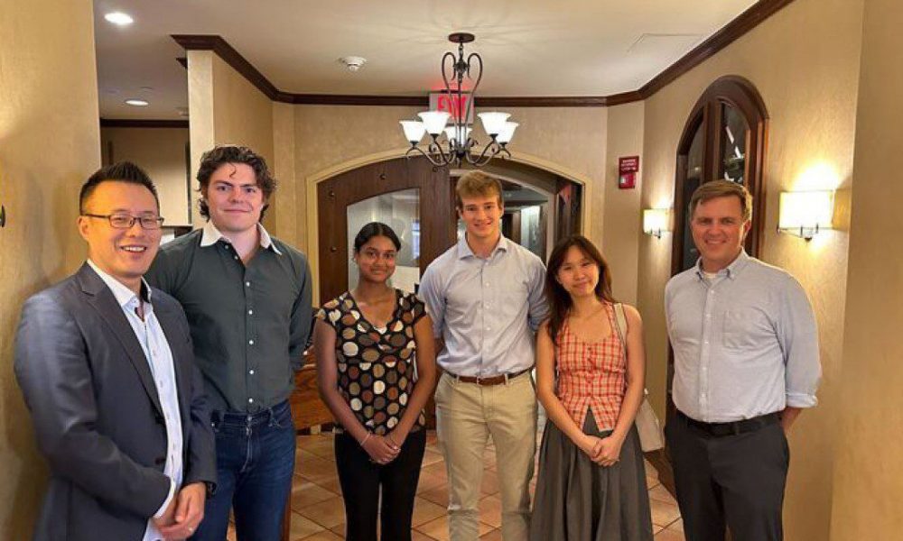 Group of people standing in a cream colored hallway looking happy.