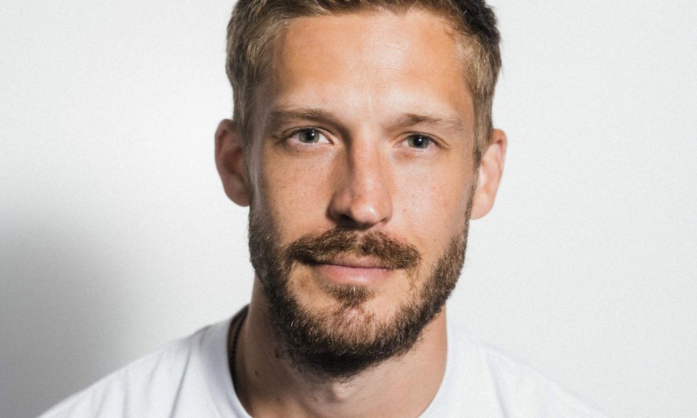 up close photo of blond haired man with facial hair wearing white shirt