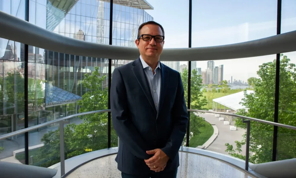 Man wearing dark suit and glasses standing in front of round glass wall skyscraper background