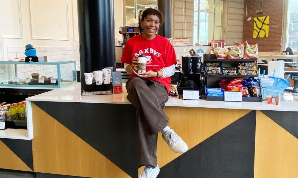 Woman sitting on a coffee shop counter holding a to-go cup of coffee