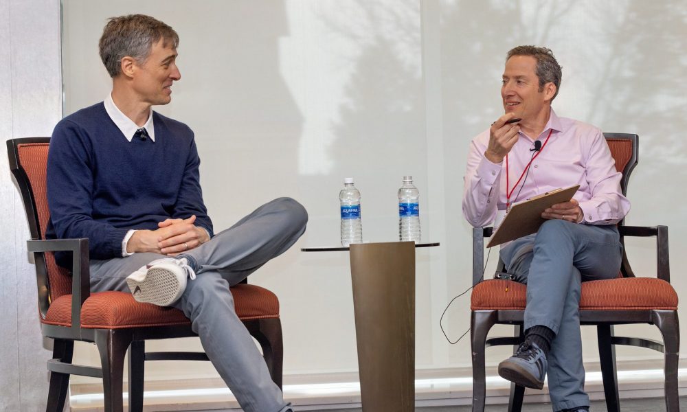 Two men sitting in chairs looking at each other with water bottles on a table between them.