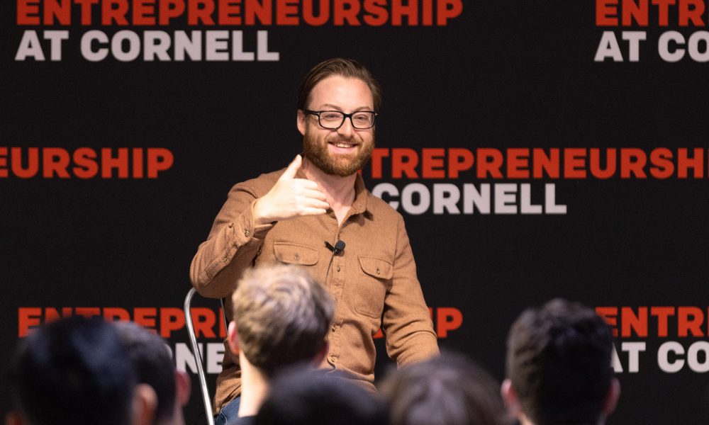Man wearing brown shirt sitting in front of a crowd of people.