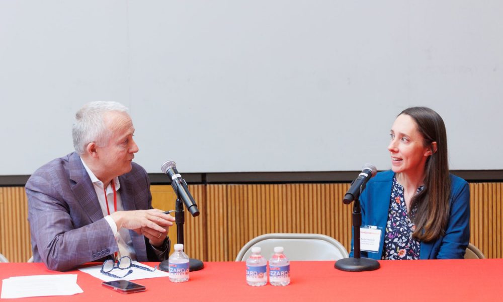 man and woman sitting at a table, both speaking into a microphone