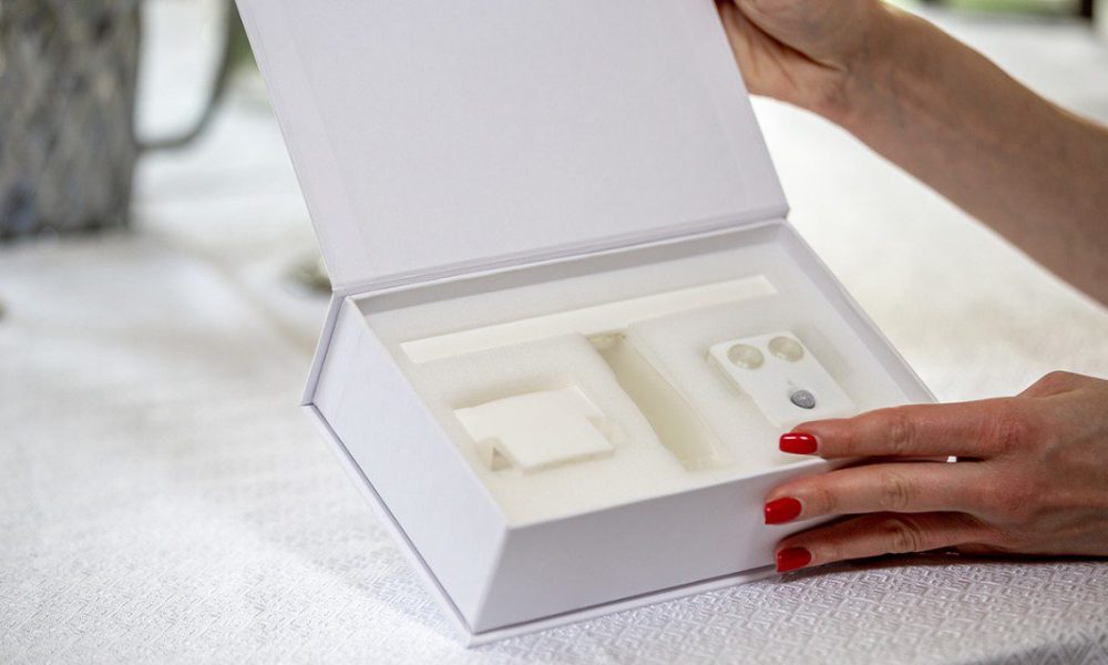person with red fingernails holding an open white box with tech care items inside