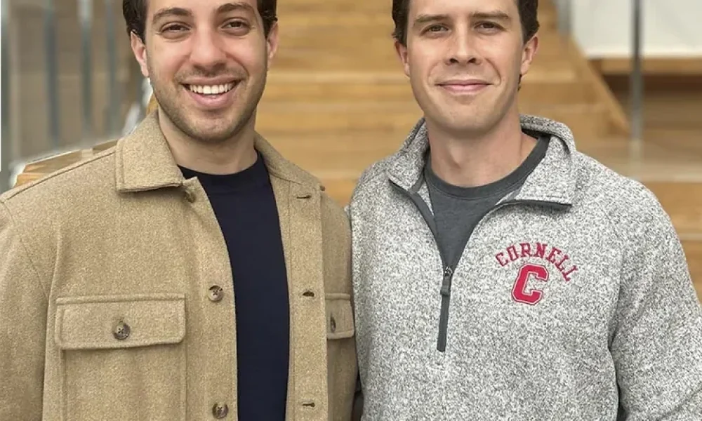 two dark haired men standing in front of staircase