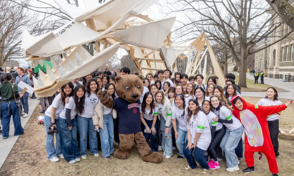 College students standing with Cornell University mascot, Touchdown the Bear underneath sculped dragon