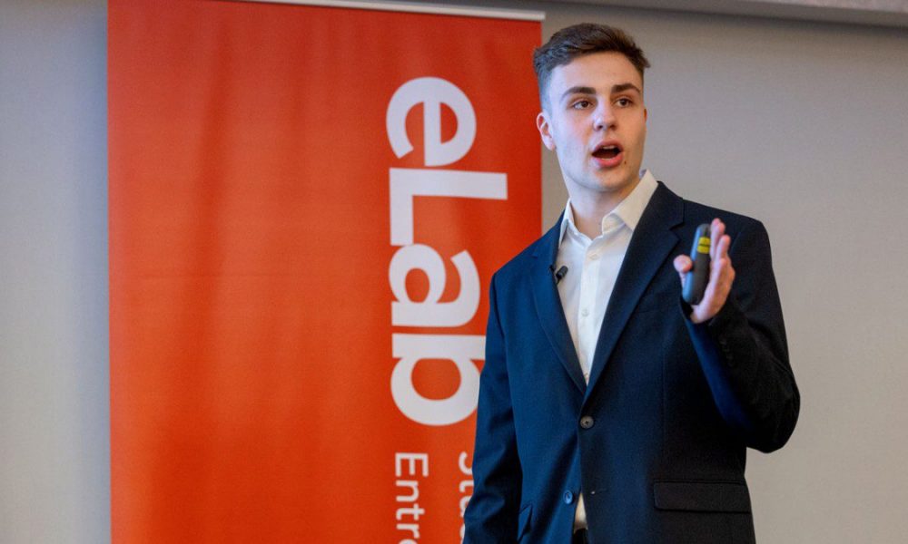 Man in business suit holding remote standing in front of a red vertical banner