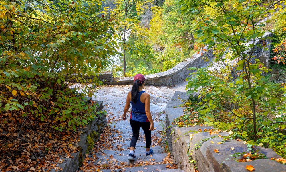 person walking in an autumn trail wearing a blue tank top, black pants and a red ball cap.