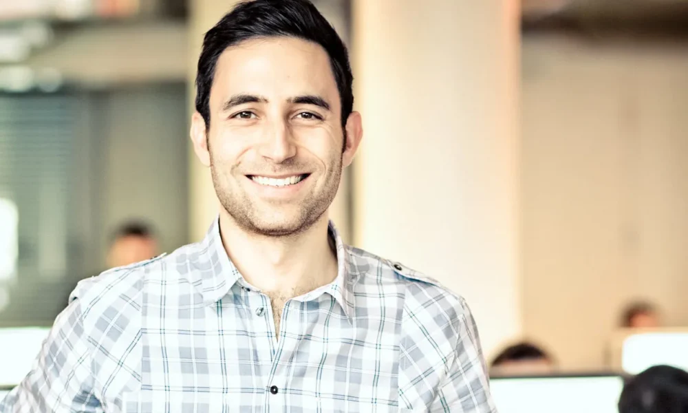 Image of Founder Scott Belsky wearing a plaid shirt with an office space in the background