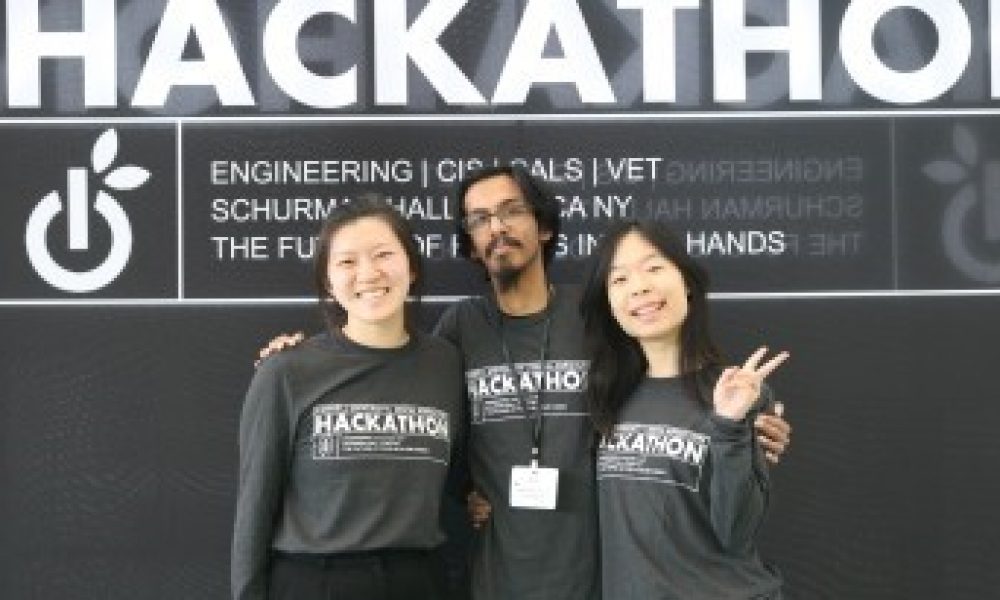 Three people wearing digital ag hackathon shirts standing in front of hackathon banner