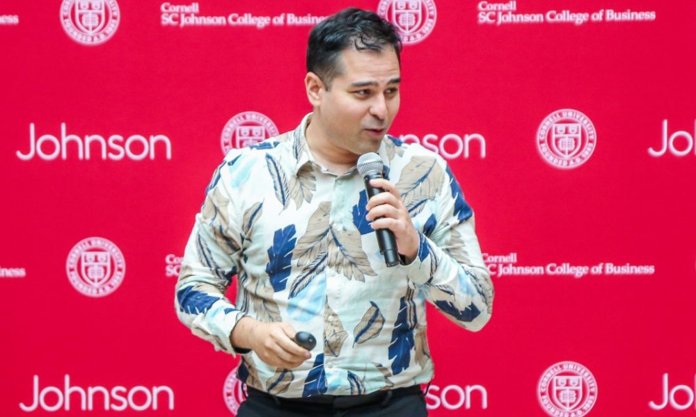 man wearing tropical blue shirt speaking into microphone standing in front of Johnson backdrop