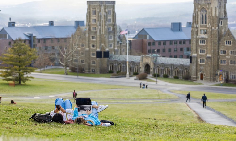 two people lying on sloped hill with Cornell college campus buildings in background