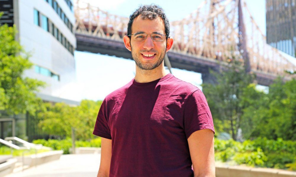 man standing outside near a bridge wearing a maroon t-shirt
