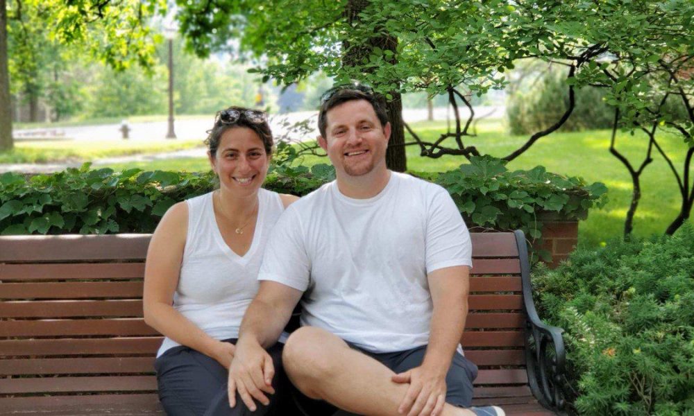 man and woman sitting on a park bench with green foliage in background