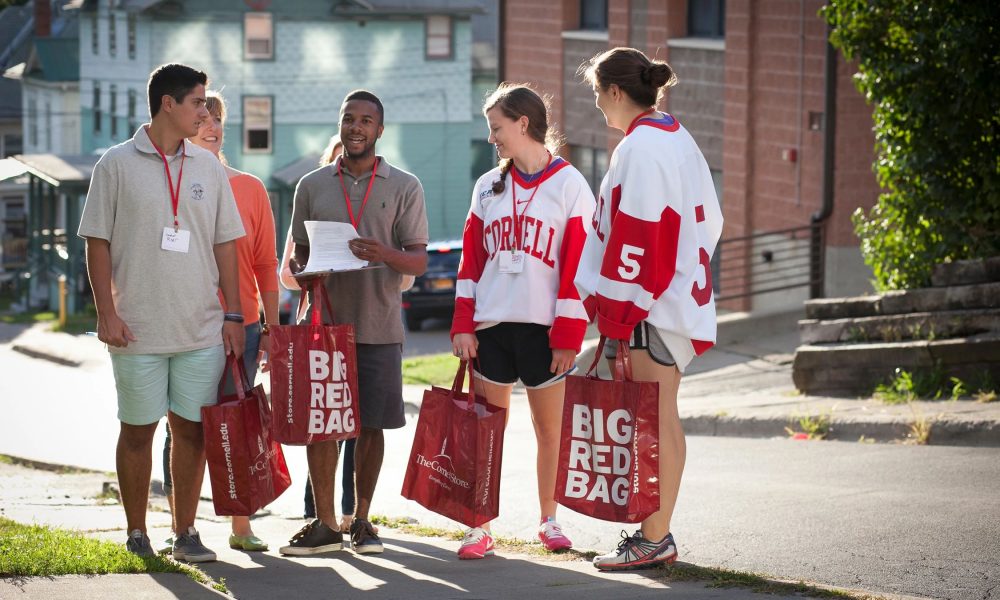 Group of students on Cornell University campus, some wearing Cornell Hockey jerseys and holding red Big Red Bags.