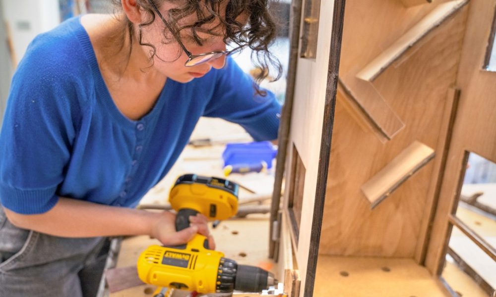 woman wearing a blue shirt and using power tools to build wooden unit