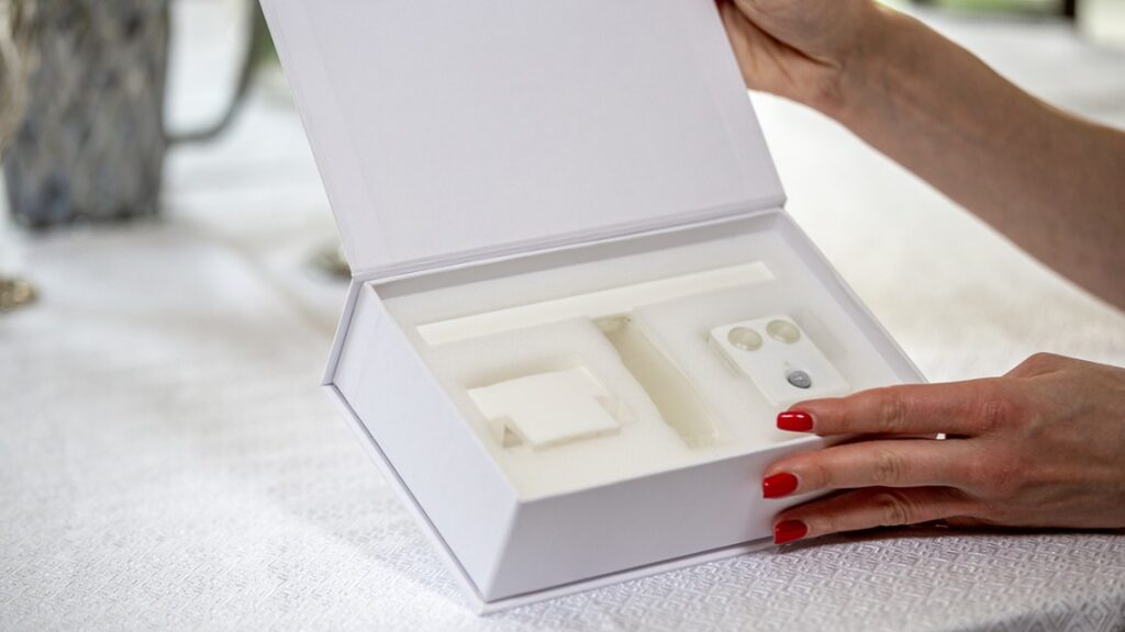 person with red fingernails holding an open white box with tech care items inside