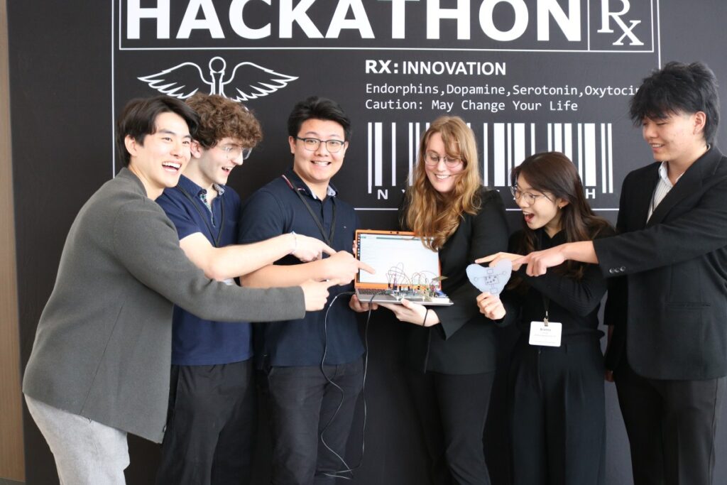 Six students standing in front of Health Hackathon backdrop excited to show off their project they worked on during a team at Health Hackathon event