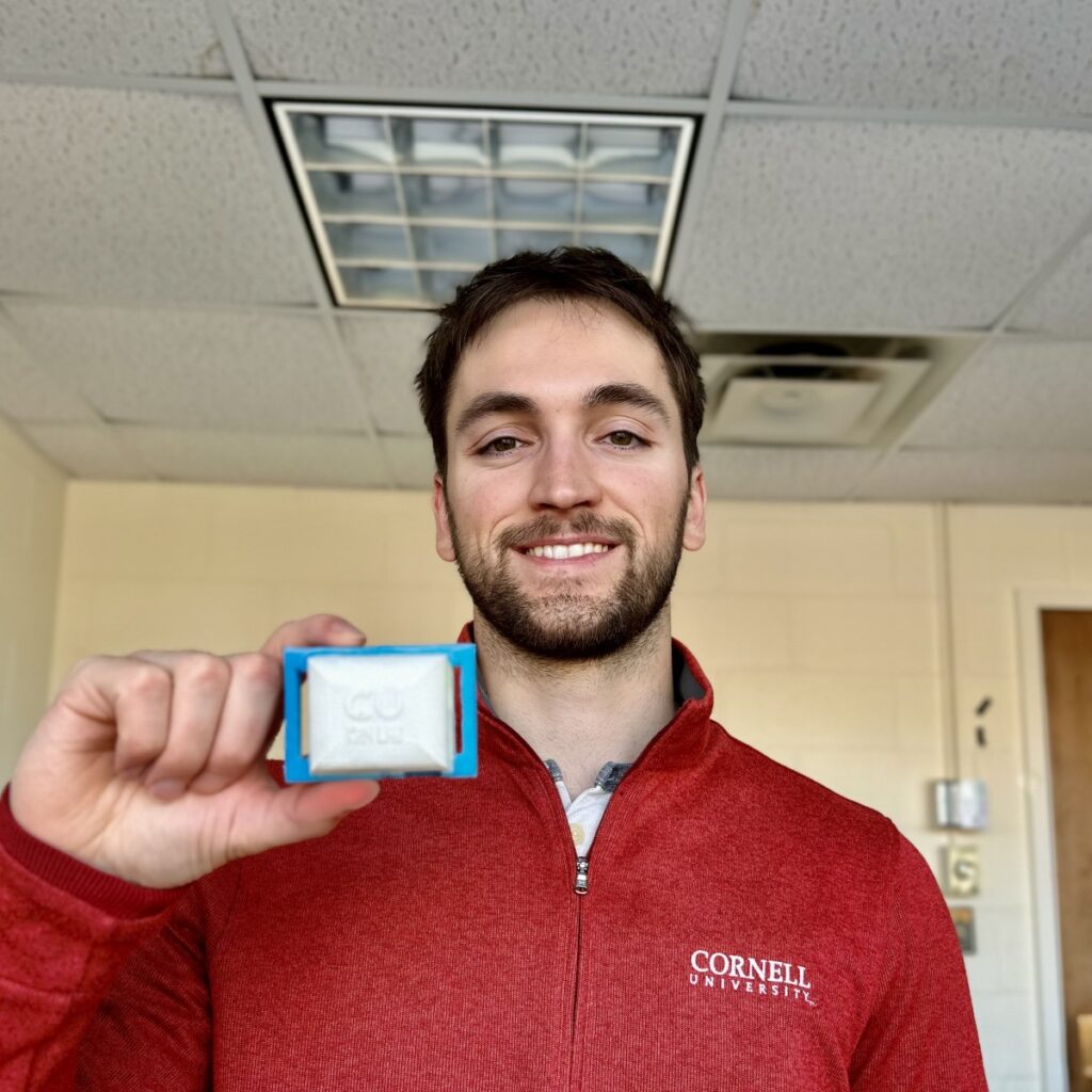 Man wearing red quarter zip pullover with Cornell logo on pocket area, holding up his designed heart sensor