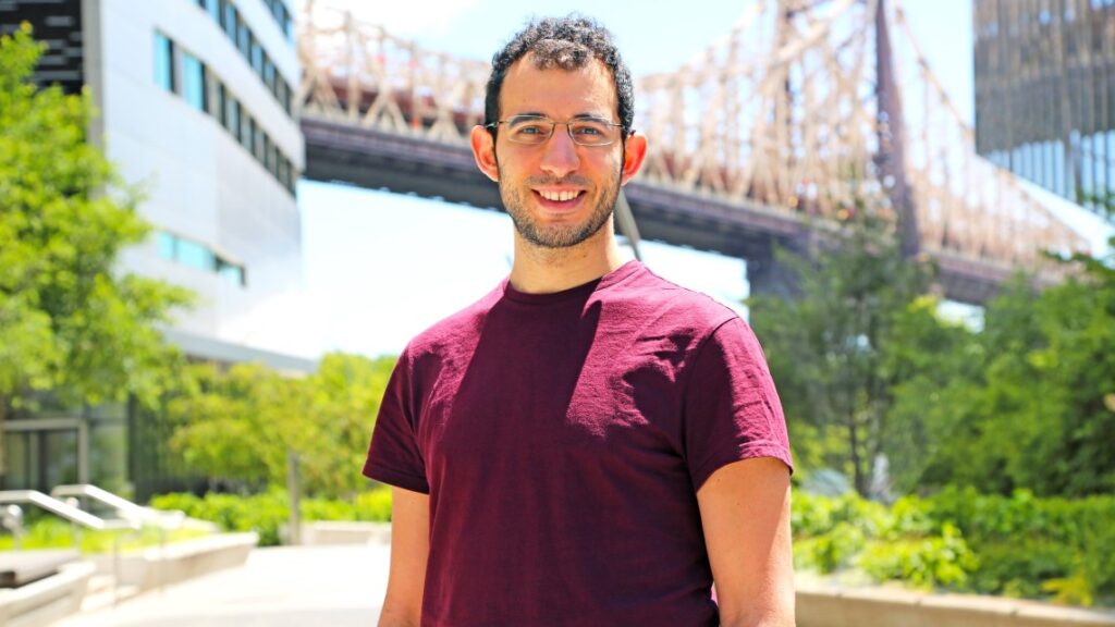 man standing outside near a bridge wearing a maroon t-shirt