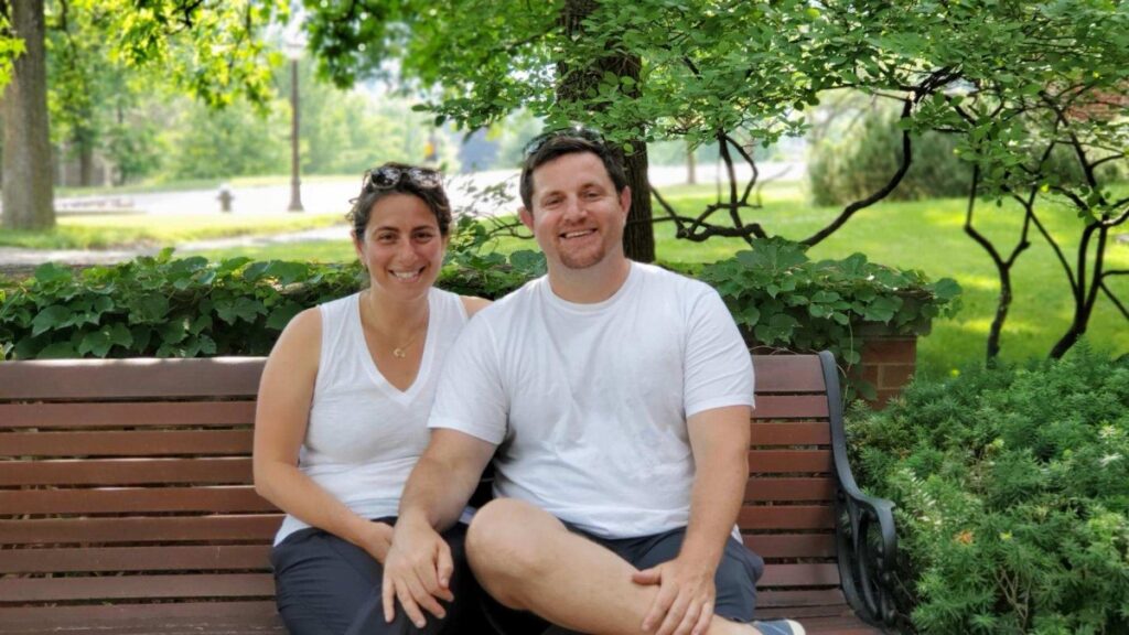 man and woman sitting on a park bench with green foliage in background