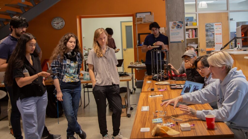 multiple people in an orange room standing around a wooden table with people sitting at the table