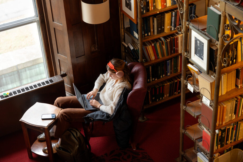 student studying in comfortable lounge chair near window in library, wearing red headphones